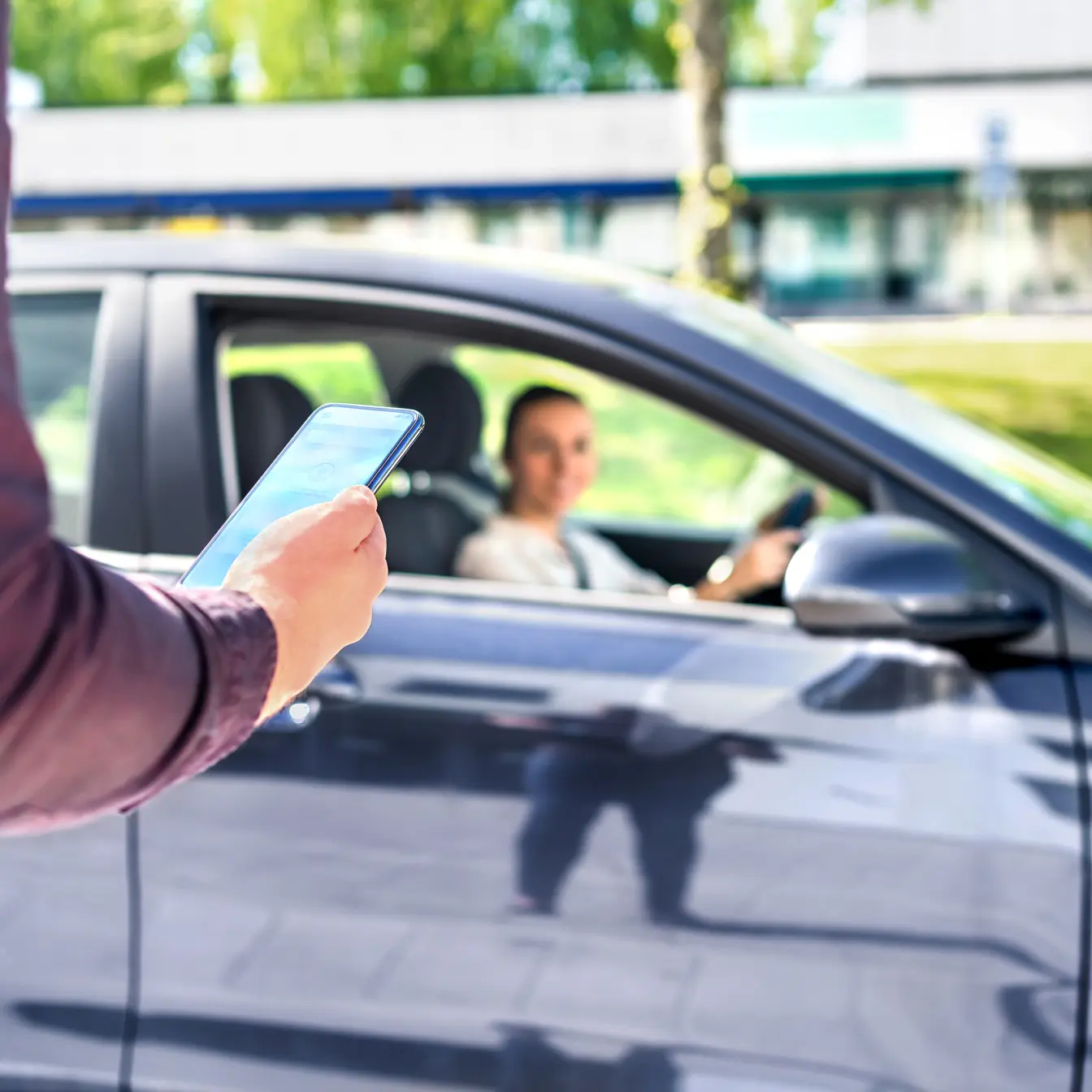 Mann mit Telefon in der Hand, im Hintergrund eine Frau, die ein Auto fährt