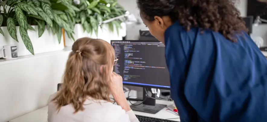 Zwei Frauen betrachten Code auf einem Monitor